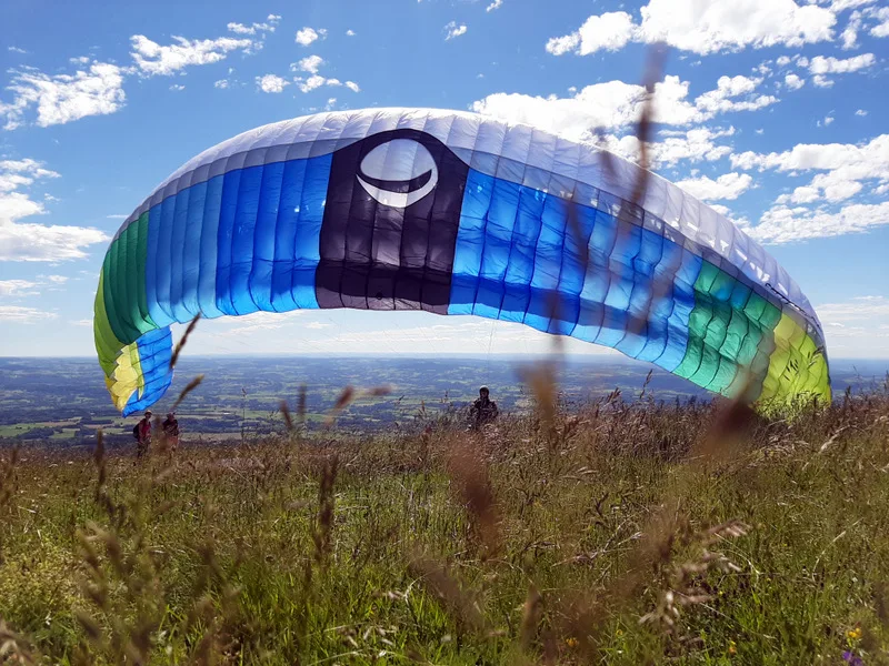 gonflage d'une voile de parapente de toute les couleurs dans de l'herbe haute, ciel bleue avec quelques nuages