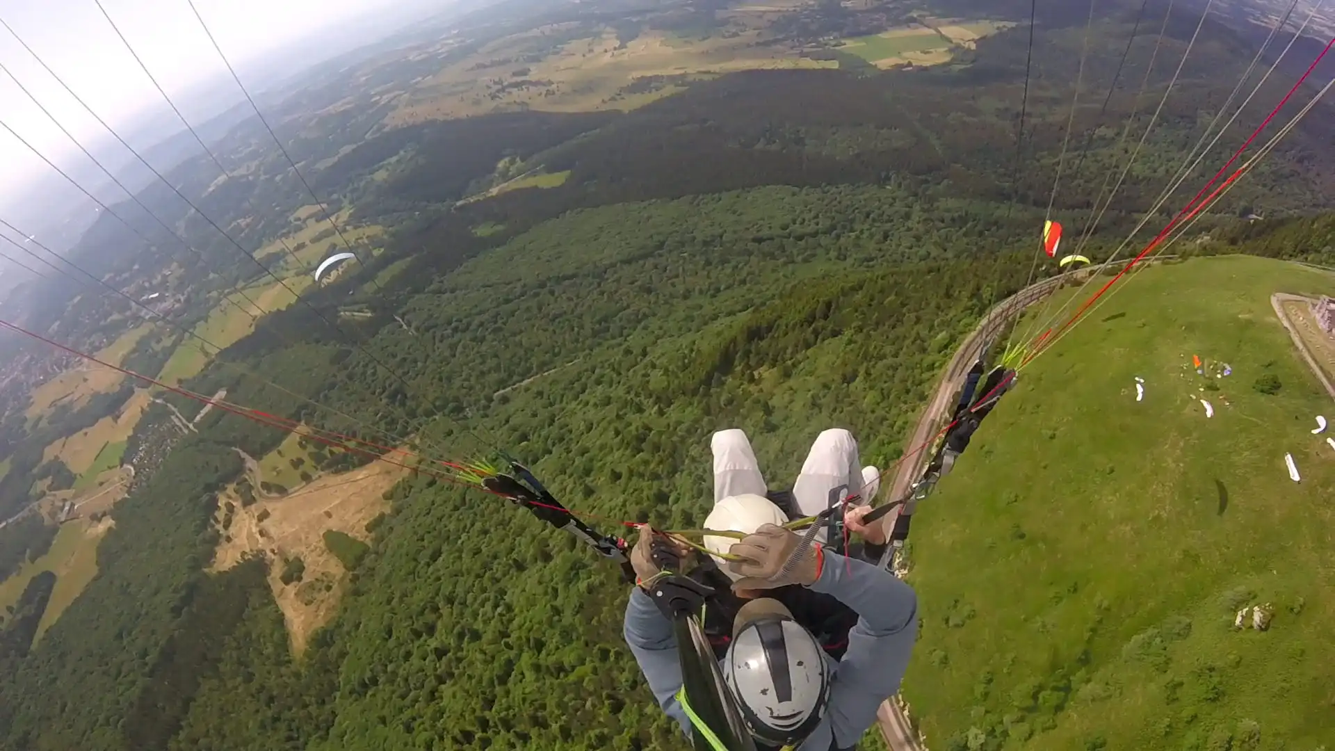 Vue aérienne depuis le vol montrant les autres voiles de parapente se préparant au loin sur le sol